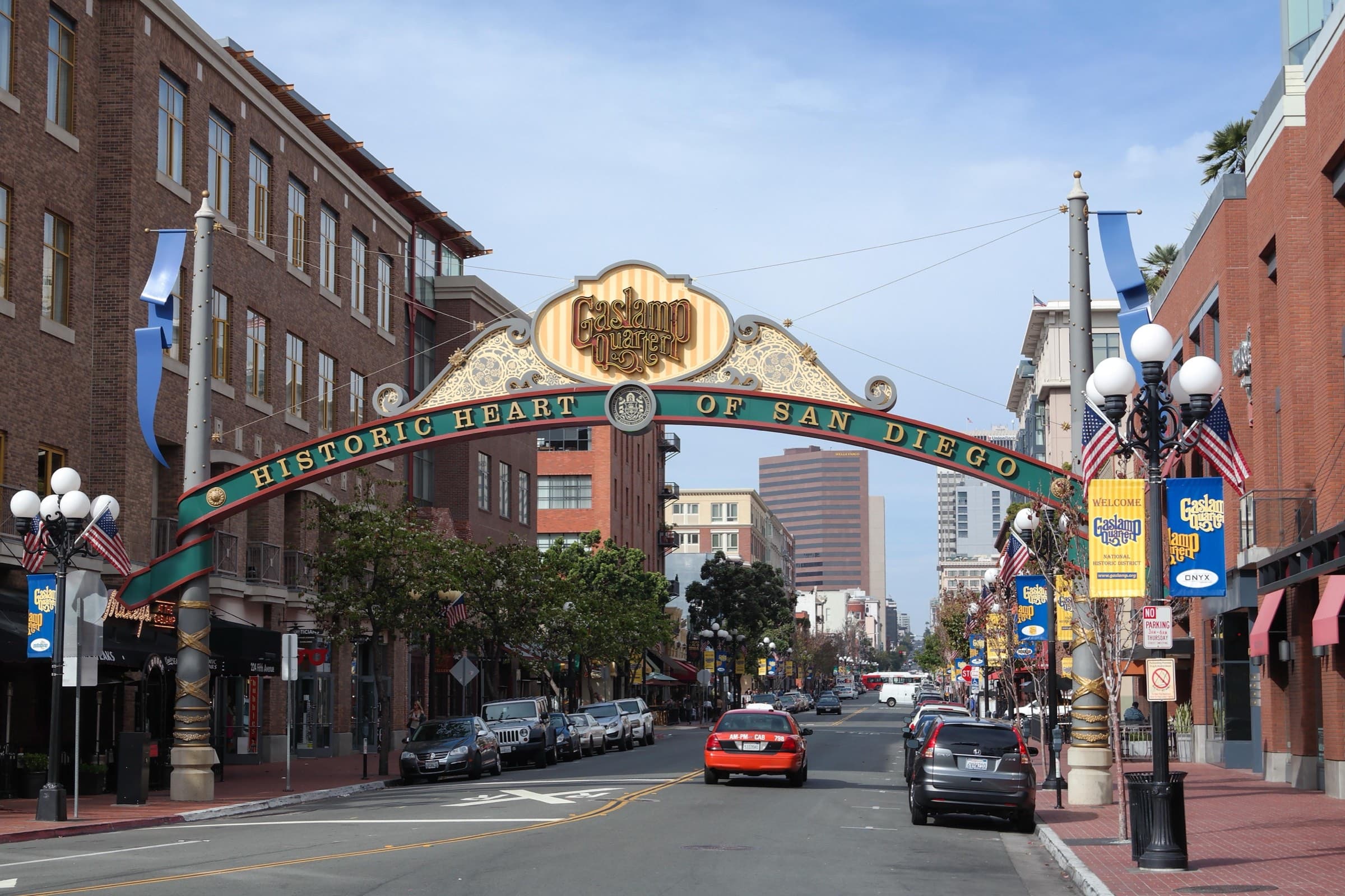 The Gaslamp Quarter arch reading Historic Heart of San Diego over Fifth Avenue, with red-brick buildings, globe streetlamps and downtown towers beyond